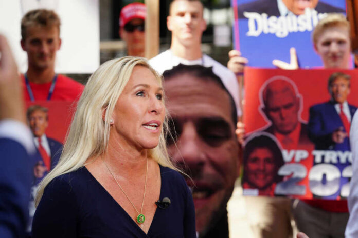 Woman speaking at outdoor event with protest signs in background