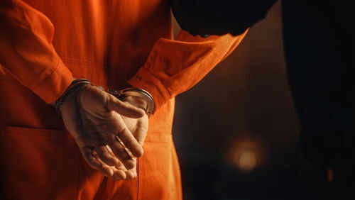 Person in orange jumpsuit with hands cuffed behind back