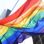 Activists Demand Emergency; Mayor Pumps Brakes A vibrant rainbow flag waving against a city backdrop