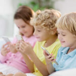 Three children sitting together, each using a smartphone