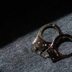 A pair of handcuffs resting on a dark surface with light casting a shadow