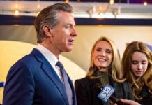 Grand Jury Fury—Newsom Points At Trump A man speaking at a public event with two women smiling nearby