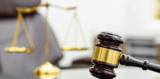 A wooden gavel resting on a sound block with a blurred scale of justice in the background
