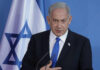 Man speaking in front of Israeli flag backdrop