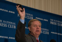 One Senator’s Death Reignited Bitter Divisions Man holding phone at National Press Club event