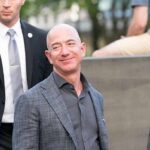 bald man in a gray suit smiling outdoors