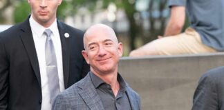 bald man in a gray suit smiling outdoors