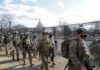 Soldiers in riot gear patrol near a fenced government building