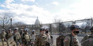 Soldiers in riot gear patrol near a fenced government building