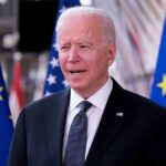man in suit speaking between EU and US flags