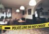 Epstein-Linked Model Scout Found Dead In France Police tape blocks entrance to a dimly lit restaurant interior