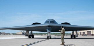 A military personnel stands in front of a B-2 Spirit stealth bomber on an airfield