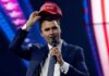 Man in a suit holding a red cap while speaking into a microphone