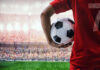Soccer player holding a ball in a stadium with a cheering crowd
