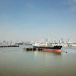 Cargo ship docked in harbor with city skyline in background