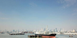 Cargo ship docked in harbor with city skyline in background