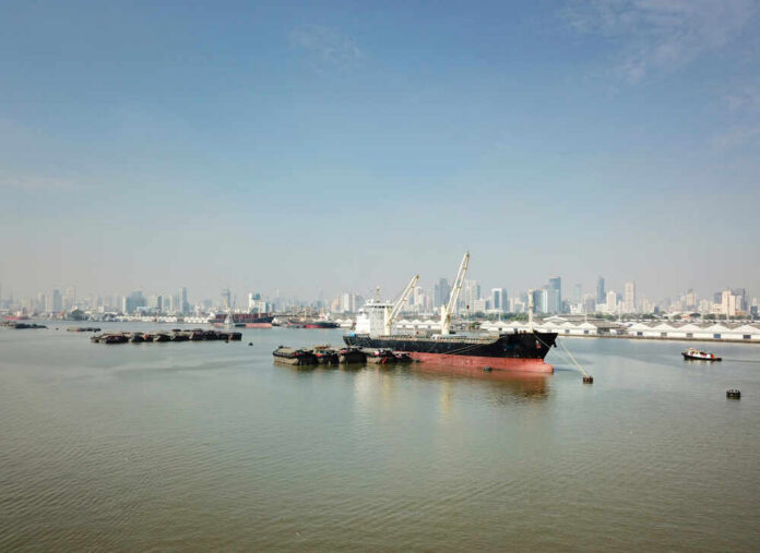 Cargo ship docked in harbor with city skyline in background