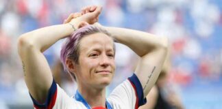 Soccer player with purple hair smiling with hands on head