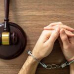 Handcuffed hands beside a judge's gavel