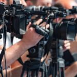 When The System Couldn’t Take The Heat television cameras on tripods at a media event