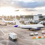 Airplanes at airport gates during sunset with ground vehicles and jet bridges