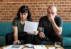 Two adults on a sofa reviewing bills and using a calculator