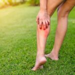 person holding calf with red irritated skin on a grassy lawn