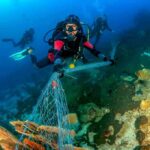 Scuba diver removing fishing net from coral reef