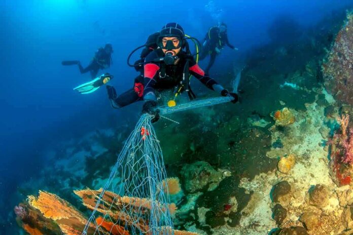 Scuba diver removing fishing net from coral reef