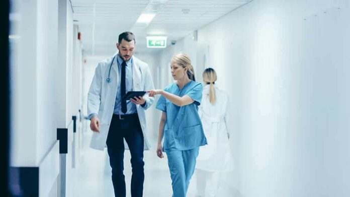 Doctor and nurse walking in a hospital corridor reviewing a tablet