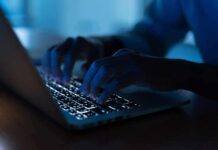 Hands typing on a backlit laptop keyboard at night