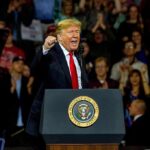 Donald Trump speaking at a rally behind a presidential podium