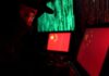 Hooded person using a laptop with Chinese flags on screens