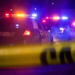 Police cars with flashing lights behind yellow caution tape at night
