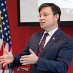Man in suit speaking at podium with US flag in background