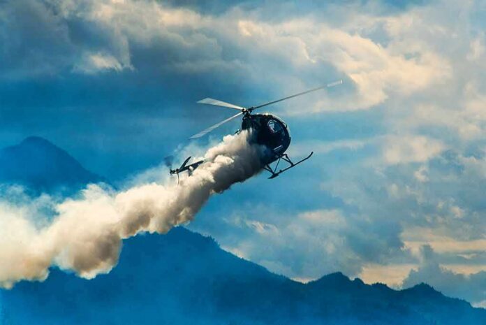 Helicopter releasing smoke over mountains
