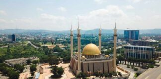 Golden-domed mosque with four minarets in a modern cityscape