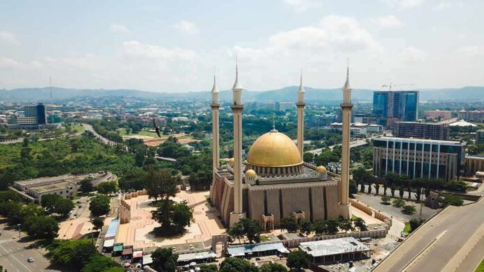 Golden-domed mosque with four minarets in a modern cityscape