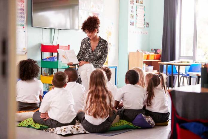 Teacher reading a book to a group of young students on the classroom floor