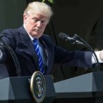 Donald Trump speaking at dual podiums with arms outstretched