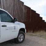 Border patrol SUV parked beside tall steel border fence