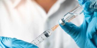 Gloved hands drawing liquid into a syringe from a vial