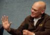 James Carville speaking into a handheld microphone, gesturing with his left hand