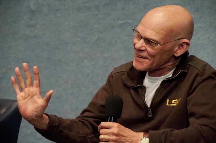 James Carville speaking into a handheld microphone, gesturing with his left hand