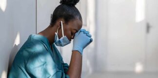 Healthcare worker in scrubs sitting against a wall with head bowed