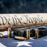 Felon Gun Ban Faces Full-Force Review Handgun and bullets on American flag with rolled parchment