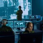 Military analysts monitor data on multiple screens in a command center