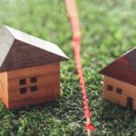 Two wooden house models separated by a red boundary line on grass