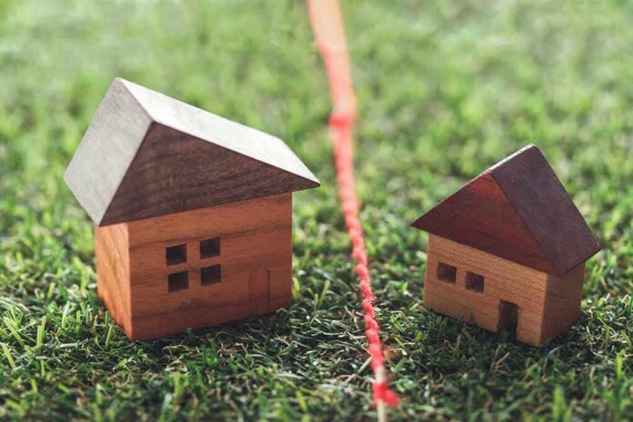 Two wooden house models separated by a red boundary line on grass