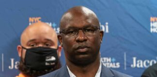 Man in suit and glasses at a press conference